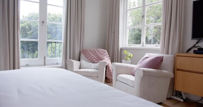 Camera is panning right after low-angle hold, revealing bed front, armchairs and plant by windows