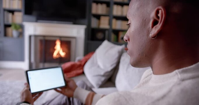 Man holding tablet, tapping, swiping, checking content on sofa by fireplace, copy space