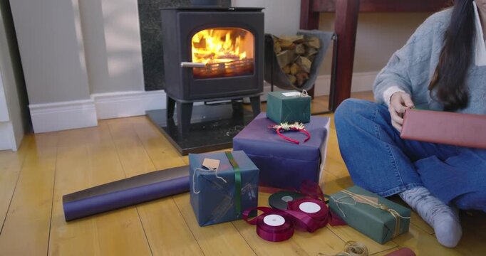 Asian woman sitting by wood stove, preparing gifts, wrapping with ribbons and twine, copy space