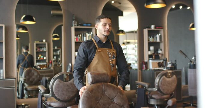 African American man standing behind chair hands on headrest in salon aproned awaiting client