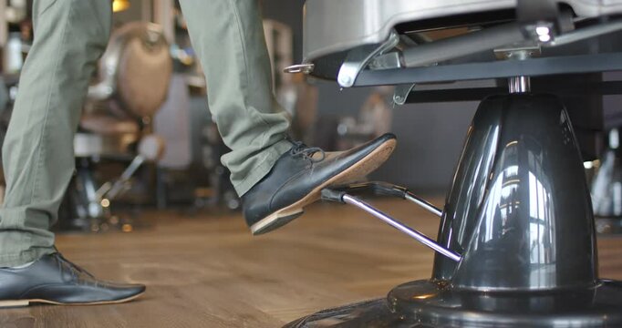 Man stepping from left, repeatedly pressing salon chair pedal, adjusting height, copy space