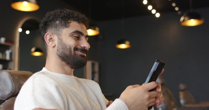 African man sitting in leather chair, reacting to message on smartphone, smiling toward camera