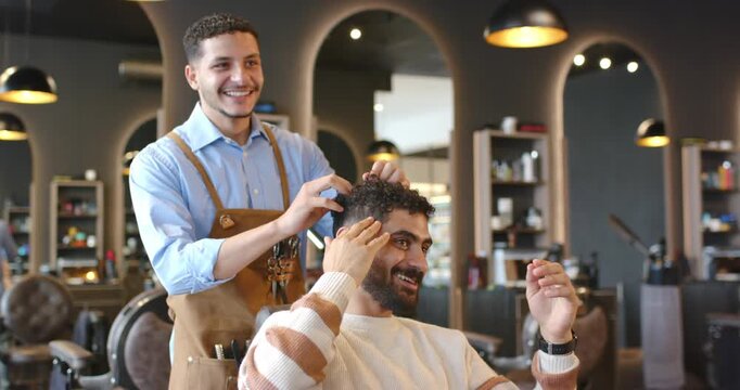 African American male barber wearing apron placing hands on client styling hair to shape at salon