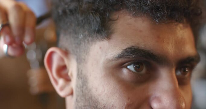 Adult male getting haircut at salon, barber hand coming with scissors trimming temple edge for fade