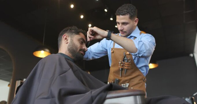 Barber trimming hair with client reclining, refining hairline with scissors at barbershop