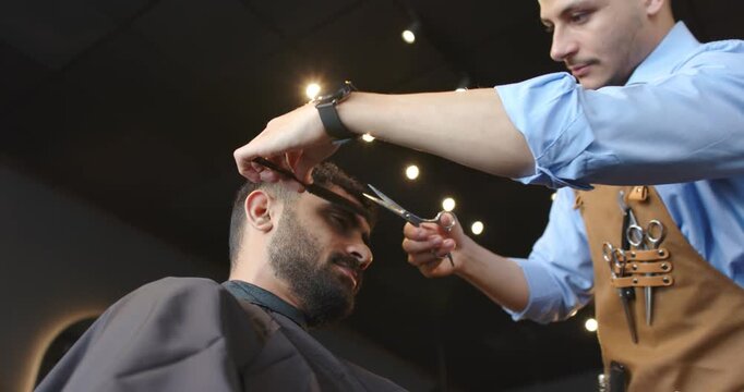 Barber trimming client, lifting hair with comb and scissors to finish haircut at shop, copy space