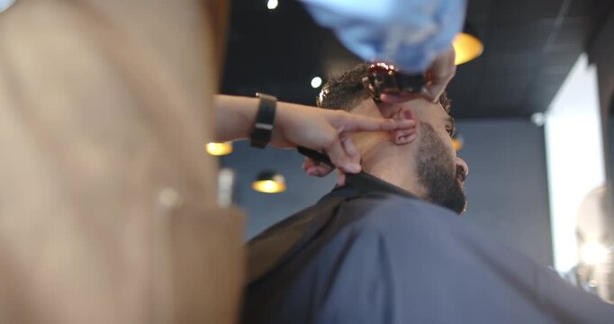 African American man in chair, tilting head, barber trimming nape with clippers at shop blending