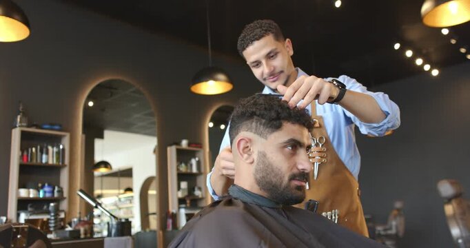 Barber combing and trimming client seated requesting trim at shop using comb, clippers, apron