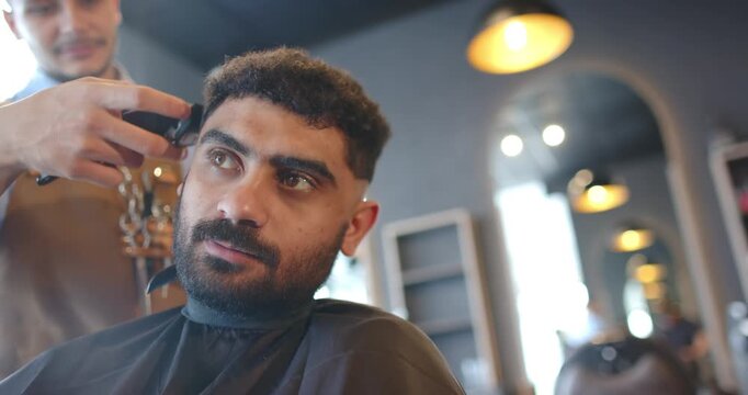 African American barber and client, barber bringing clippers shaping fade temple to crown in salon