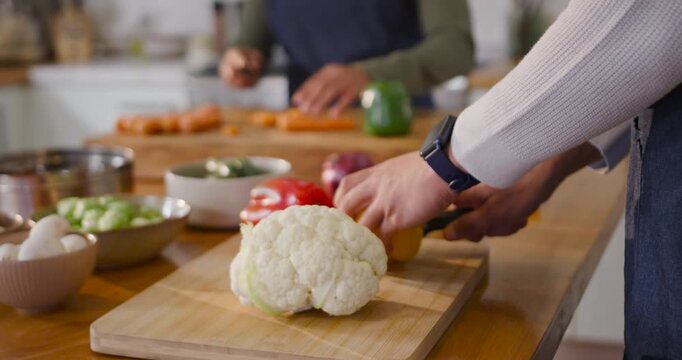 African American couple reaching for yellow pepper, chopping cauliflower in kitchen, cooking dinner