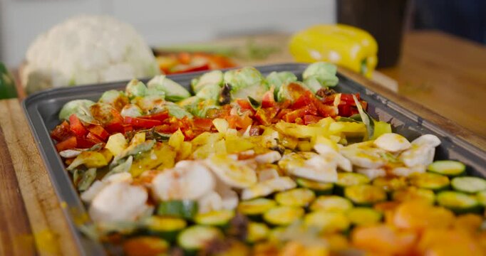 Camera shifting focus and angle to reveal roasting tray holding seasoned vegetables on wooden board