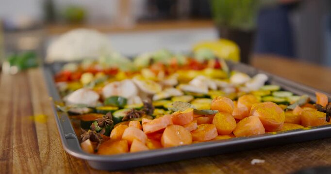 Camera is pulling focus, revealing seasoned vegetable tray on wood board ready for roasting