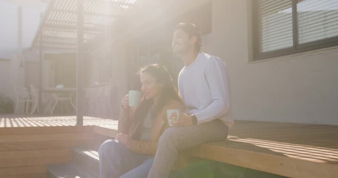 African American couple sitting on steps man smiling, woman having coffee from mug sunlight flaring