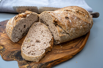 Naklejka premium Rustic walnut country loaf on wooden board, crusty and flour-dusted with visible walnut pieces, ready to slice with serrated knife, warm, homemade, artisanal bread.
