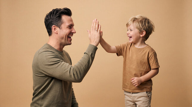 A happy father and young son exchange a high five in a clean studio setting, representing celebration, encouragement, teamwork, and joyful parenting.