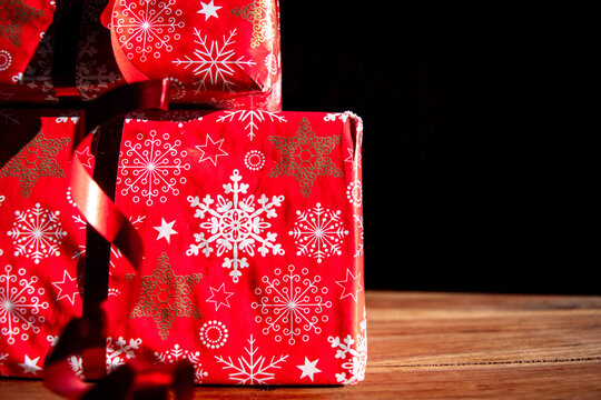 Wrapped Christmas gift boxes with red snowflake paper on a wooden surface against black background