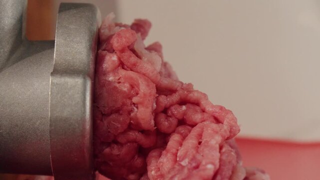Industrial style raw beef extrication with textured details and sheen. Macro shot capturing coarse pink strands of raw beef moving through metal grinder