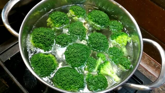 A metal pot of boiling water containing bright green broccoli florets sits on the stove, conveying the impression of a fresh and healthy cooking process.