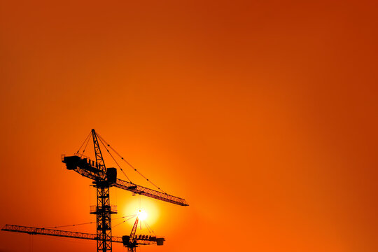 Silhouetted cranes against a vibrant orange sunset sky.