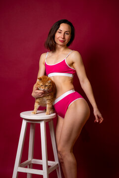 Woman in Pink Lingerie Holding Ginger Cat on Stool