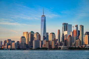 Fototapeta na wymiar One World Trade Center and Lower Manhattan skyline at sunset. Skyscrapers of New York City reflecting warm golden hour sunlight with ripples on the river water.