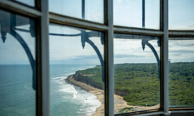 Fototapeta premium View through a window of a bronze statue in Montauk. A dark stone frame surrounds a glass window overlooking a monument near the ocean waves.