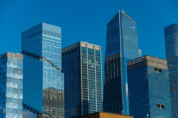 Fototapeta premium Modern glass skyscrapers rise into blue sky in New York. Tall contemporary corporate buildings with reflective windows under clear sunny weather.