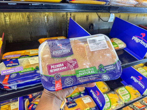 Hand holding a tray of Pilgrims JBS chicken breast inside a Walmart supermarket. Background shows a refrigerator filled with trays of various chicken cuts. Jalisco, Mexico July 11 2026.