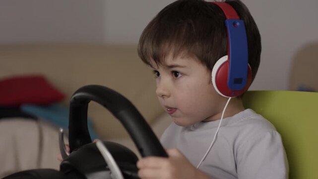 Boy Playing Racing Video Game in Game Console. Child Playing Computer Game in Headphones With Steering Wheel. Gamer With Headset Holding Steering Wheel Playing Video Game. Kid Gambling Addiction.