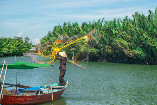 Vietnamese fisherman casting a large yellow net from a traditional wooden boat