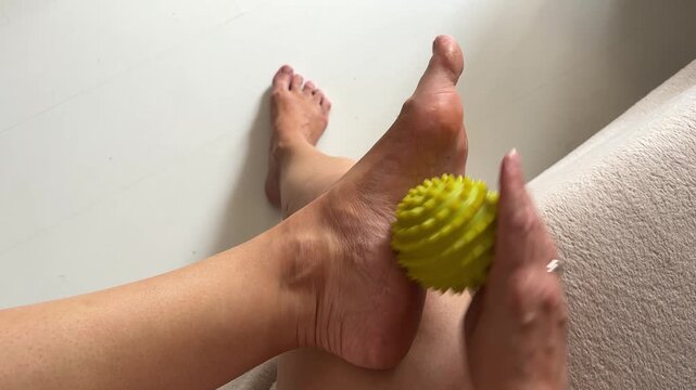 Woman massaging her foot sole with a yellow spiky massage ball