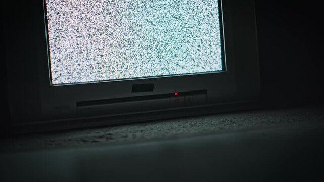 An old CRT television sits on a dark floor displaying flickering static white noise on the screen. Concept of horror, no signal glitch, retro technology, and eerie vintage atmosphere.