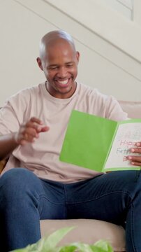 Vertical video: Kid giving Fathers Day card, father in beige tee reading, smiling, placing by plant