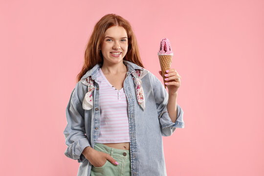 Happy teenage girl with delicious ice cream in waffle cone on pink background