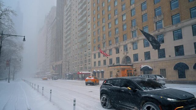 New York, USA, 25 December 2025 : Snowstorm along an Upper East Side Manhattan avenue. Cars pass apartment facades and hotel flags through windblown snow in Manhattan.