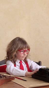 Funny kid pretending to be a businessman. A little child is playing in the office with a vintage typewriter and a retro telephone. Vertical video, slow motion