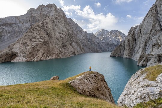 Tourist at the blue mountain lake between rocky steep mountain peaks, Kol Suu Lake, Sary Beles Mountains, Naryn Province, Kyrgyzstan