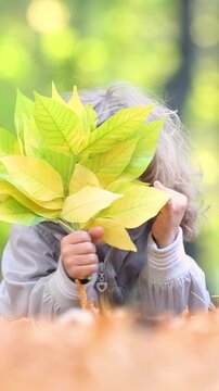 A happy child is playing hide-and-seek outside in an autumn park. A little girl is having fun outdoors. Vertical video, slow motion