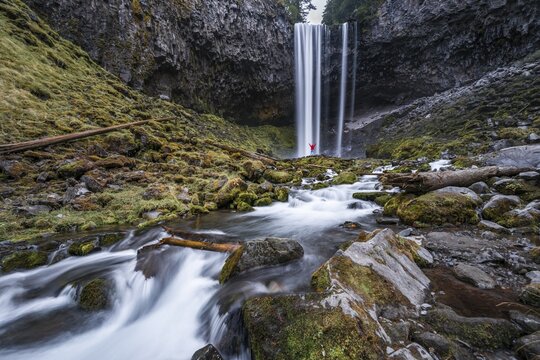 Hiker in front of a high waterfall, water falls over a rocky outcrop, Tamanawas Falls, wild river Cold Spring Creek, time exposure, Oregon, USA