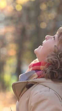 A happy child is standing  outside in an autumn park. A little girl is having fun outdoors. Vertical video, slow motion
