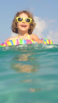 A happy child is having fun at the beach during the summer holidays. Funny girl enjoying a vacation in the sea. Slow motion, vertical video