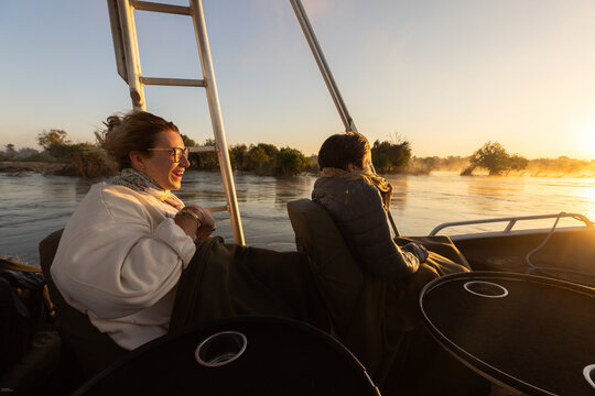  young people experiencing cold sunrise on the Zambezi River, as fog rises from the water, Zimbabwe, Africa