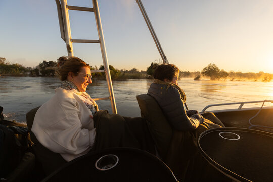  young people experiencing cold sunrise on the Zambezi River, as fog rises from the water, Zimbabwe, Africa