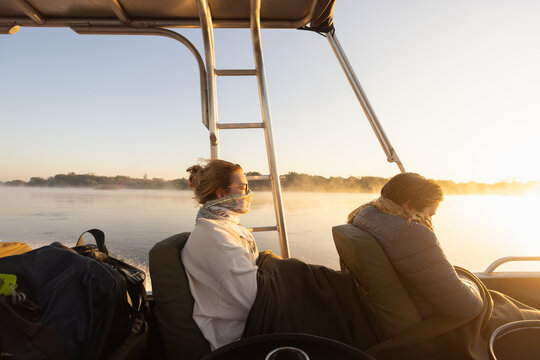  young people experiencing cold sunrise on the Zambezi River, as fog rises from the water, Zimbabwe, Africa