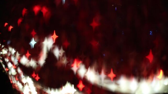 Glowing red four-pointed star bokeh lights on dark background with white diagonal light trail, festive holiday celebration and Christmas abstract sparkle decoration.