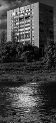 Fototapeta premium Urban residential building towering over a tranquil river, its windows catching and reflecting the bright sunlight, creating a dynamic interplay of light and shadow on the water surface