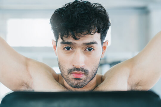 Fitness concept. Young man front view arms raised shirtless home exercise fitness routine focused face indoor exercise workout healthy lifestyle