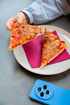 Hand holding pizza slice on break with smartphone