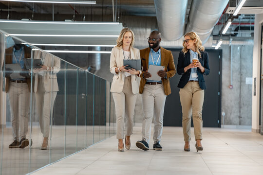 Three colleagues walking and discussing work in a modern office corridor with tablets