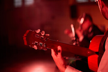Cinematic close-up classic guitar during a live stage performance with warm red lighting and blurred musicians in the background. Ideal for concerts, festivals, live music © m.zh